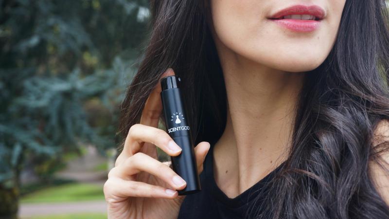 A woman holding ScentGod perfume to her neck